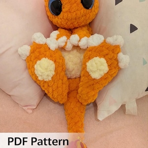 May include: An orange crochet creature with large blue eyes and white accents on its feet. The creature has a long tail with red and yellow strands. The text "PDF Pattern" is displayed on the image.