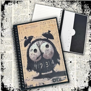 May include: A spiral-bound notebook featuring a graphic of a black owl-shaped alarm clock on a tan, newspaper-style background. The clock face displays the numbers 9, 2, 3, and 4. The notebook includes lined pages and a black and white inner pocket.
