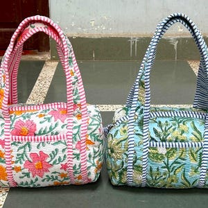 Puede incluir: Dos bolsos tote con estampado floral. Uno tiene un fondo blanco con flores rosas y naranjas, y asas a rayas rosas. El otro tiene un fondo azul claro con estampados florales amarillos y verdes, y asas a rayas azules.