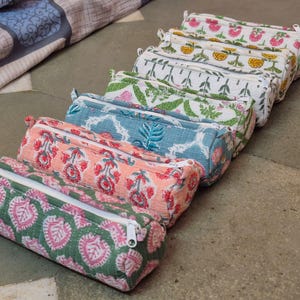Può includere: Una collezione di astucci colorati e fantasia. Ogni astuccio presenta un design floreale o a foglie unico nei toni del rosa, verde, blu e giallo. Gli astucci hanno una forma rettangolare con chiusura a cerniera.