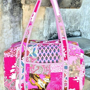 Può includere: Borsa tote patchwork rosa con motivi floreali e paisley. La borsa ha una forma rettangolare, una cerniera superiore, una tasca frontale e due manici lunghi con un design a righe. La borsa è realizzata in tessuto trapuntato.