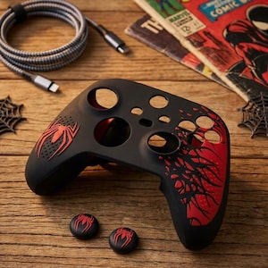 May include: Black and red Spider-Man themed video game controller with matching thumb grips. The controller has a red spider logo and web design. A black and grey cable and vintage comic books are also in the image.