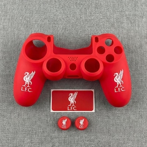 May include: A red controller skin and stickers set, featuring the Liverpool Football Club logo. The set includes a controller cover, a rectangular sticker, and two round stickers, all red with the team's emblem and "L.F.C." text.