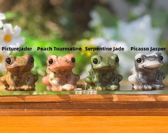 May include: Four small stone frog figurines. The frogs are made of Picturejader, Peach Tourmaline, Serpentine Jade, and Picasso Jasper. The frogs are brown, pink, green, and gray. The names of the stones are written above each frog.