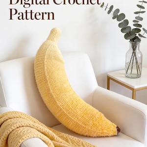 Puede incluir: Un cojín de ganchillo grande con forma de plátano amarillo, con una superficie texturizada y una pequeña punta marrón en el extremo. El texto "Digital Crochet Pattern" aparece en la esquina superior izquierda, indicando un archivo digital.