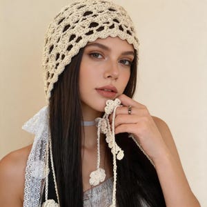 Può includere: Un cappello all'uncinetto color crema a trama aperta con un motivo floreale. Il cappello ha una corona arrotondata e un bordo smerlato. Lacci all'uncinetto color crema con accenti floreali pendono dal cappello. Un accessorio elegante.