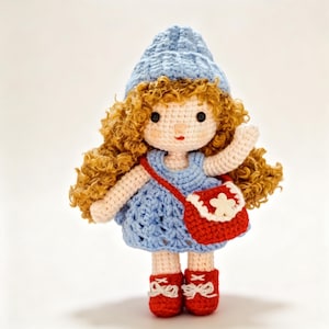 May include: A handmade crochet doll with curly, light brown hair, wearing a light blue dress and matching hat. The doll has a red purse with a white flower and red shoes with white bows. The doll is approximately 8 inches tall.