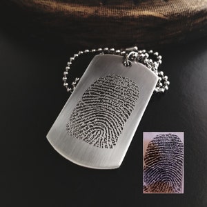 May include: A silver dog tag necklace with a fingerprint engraved on the front. The tag is hanging from a silver chain.