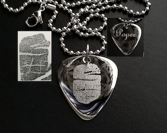 May include: A silver guitar pick necklace with a personalized fingerprint design and the name "Popeye" engraved on the pick. The necklace is on a silver ball chain.