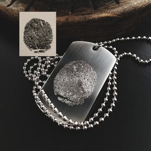 May include: A silver dog tag necklace with a fingerprint design engraved on the front. The necklace is made of a silver chain.