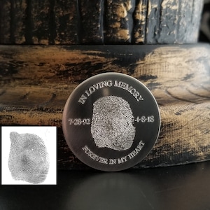 Op de afbeelding: Zilveren gedenkmunt met een vingerafdrukdesign, de tekst "In Loving Memory 7-28-92 4-8-18 Forever In My Heart" is gegraveerd op de munt.