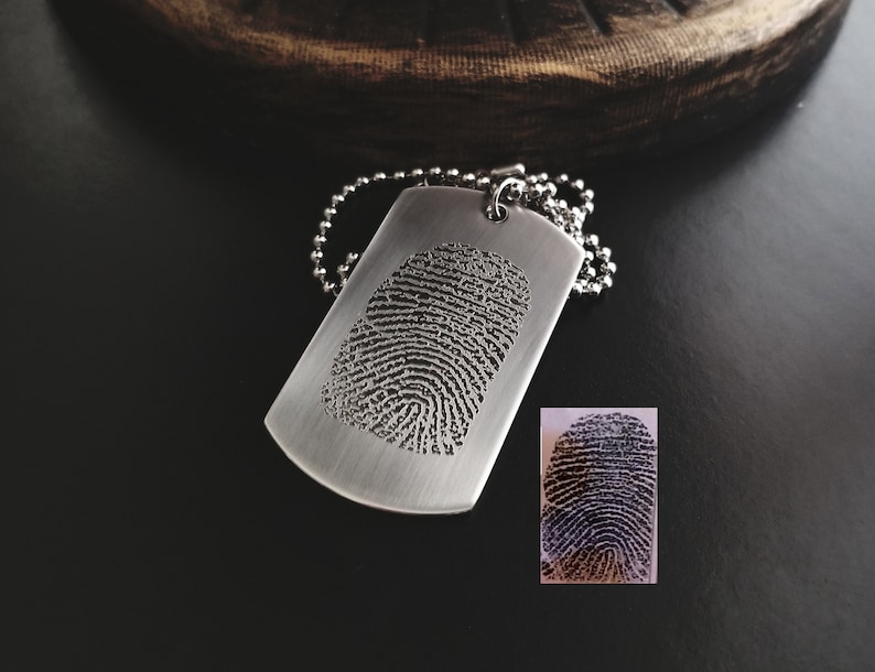 May include: A silver dog tag necklace with a fingerprint engraved on the front. The tag is hanging from a silver chain.