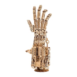 May include: A wooden model of a mechanical hand, constructed from interlocking laser-cut pieces. The hand is posed with fingers extended, showcasing intricate details of the joints and structure. The model is made of light brown wood and stands on a circular base.