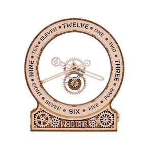 May include: A circular wooden clock with an open center featuring exposed gears and hands. The outer frame displays the numbers written as words from ONE to TWELVE. The base includes decorative gear motifs and the text WOD TRICK in a cutout style.