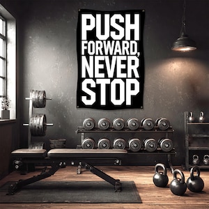 May include: A black banner with the words "PUSH FORWARD, NEVER STOP" in white lettering hangs in a gym. The gym has weights, a bench, and kettlebells. The room has a dark, industrial aesthetic.