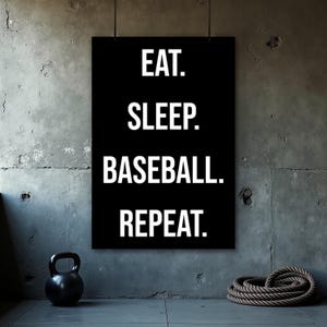 Op de afbeelding: Zwart poster met witte tekst: "EAT. SLEEP. BASEBALL. REPEAT." tegen een grijze betonnen muur. Een zwarte kettlebell en een opgerold touw zijn zichtbaar op de voorgrond.