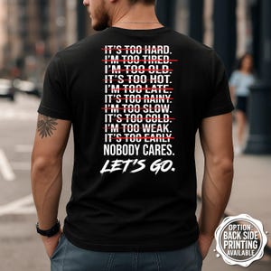 Puede incluir: Camiseta negra con texto blanco: "IT'S TOO HARD. I'M TOO TIRED. I'M TOO OLD. IT'S TOO HOT. I'M TOO LATE. IT'S TOO RAINY. I'M TOO SLOW. IT'S TOO COLD. I'M TOO WEAK. IT'S TOO EARLY. NOBODY CARES. LET'S GO." Impresión trasera disponible.