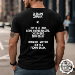 May include: Black t-shirt with white text on the back. The text reads: "DO SHARKS COMPLAIN? NO. THEY'RE UP EARLY. BITING MOTHER FUCKERS. CHASING SHIT. BEING SCARY. REMINDING EVERYONE THEY'RE A FUCKING SHARK." Option for back side printing available.