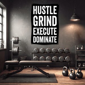 May include: A black banner with white text that reads "HUSTLE, GRIND, EXECUTE, DOMINATE" hangs on a dark gray wall. The image shows a home gym with weights, a bench, and kettlebells, suggesting a fitness theme.