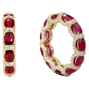 Peut inclure: Une alliance en or ornée d'une série de rubis rouge foncé taille ovale alternant avec de petits diamants blancs ronds. La bague est présentée sous deux angles, montrant la disposition circulaire continue des pierres serties en or jaune.