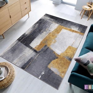 Könnte beinhalten: Ein rechteckiger Teppich mit abstraktem Design. Der Teppich zeigt eine Mischung aus grauen, weißen und goldenen rechteckigen Formen. Der Teppich ist rechteckig und scheint aus einem weichen Material zu bestehen.