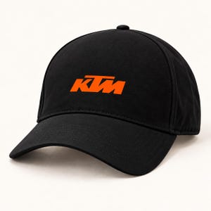 Pode incluir: Um boné de beisebol preto com o logótipo da KTM bordado em laranja brilhante na parte frontal central. O boné tem uma coroa estruturada, uma aba curva e detalhes de painéis costurados, apresentando um design simples e limpo.