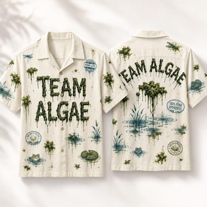 Könnte beinhalten: Ein cremefarbenes Kurzarmhemd mit Knopfleiste und einem grünen Algen-Grafikdruck. Das Design zeigt den Schriftzug "TEAM ALGAE" in einer tropfenden Schriftart sowie Illustrationen von Fröschen, Libellen und verschiedenen Teichmotiven.