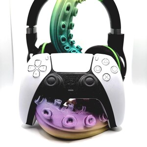 May include: A white and black PlayStation 5 controller with a gradient purple, yellow, and green octopus tentacle design. Black headphones with green accents are positioned above the controller, creating a gaming-themed display.