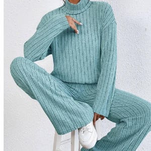 May include: A teal ribbed knit two-piece set featuring a turtleneck sweater and wide-leg pants. The outfit is made of a soft, textured fabric. The person is wearing white sneakers.