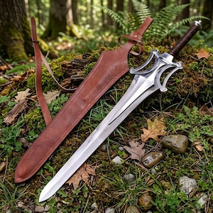 Può includere: Una spada in metallo color argento con impugnatura rivestita in pelle marrone scuro e una guardia complessa e curva. La spada è accompagnata da un fodero in pelle marrone abbinato con una tracolla in pelle regolabile integrata.