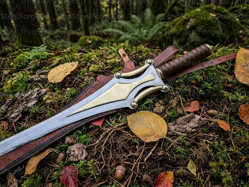 May include: A double-edged steel dagger featuring a polished brass crossguard and a brown leather-wrapped grip. The dagger rests inside a brown leather sheath with visible stitching and a leather strap, showcasing a metallic finish and brass accents.
