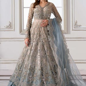 May include: A formal gown with a beige bodice and a flowing, light blue skirt. The dress features intricate silver embroidery and beadwork, with long sleeves and a matching sheer shawl. The gown has a V-neckline and a detailed, scalloped hemline.