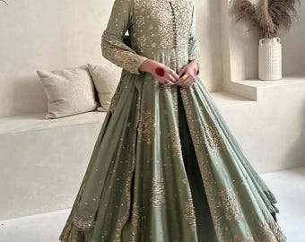 May include: Sage green formal gown with gold embroidery. The long-sleeved dress features intricate gold detailing on the bodice, sleeves, and skirt. The gown has a flowing silhouette and is suitable for special occasions.