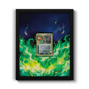 May include: A framed collectible trading card featuring a Charizard illustration, centred against a background of vibrant green flames and a dark blue starry night sky. The card is encased in a protective sleeve within a black rectangular frame.