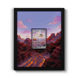 May include: A black framed display featuring a Charizard ex trading card centred over a layered paper art scene of a desert canyon with a flowing lava river, rocky cliffs, and a purple sunset sky with pink clouds, creating a 3D depth effect.