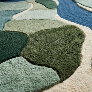 May include: A tufted rug featuring an abstract, organic pattern of interlocking shapes in various shades of green, blue, and cream. The surface has a thick, textured pile with distinct color-blocked sections separated by raised cream-colored borders.