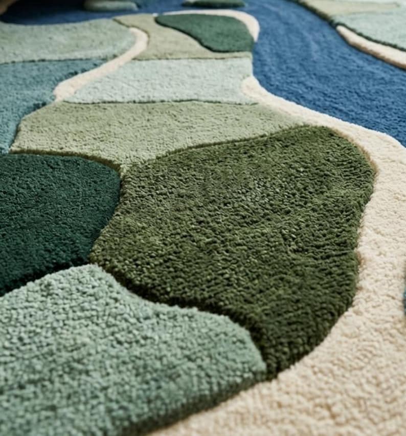 May include: A tufted rug featuring an abstract, organic pattern of interlocking shapes in various shades of green, blue, and cream. The surface has a thick, textured pile with distinct color-blocked sections separated by raised cream-colored borders.
