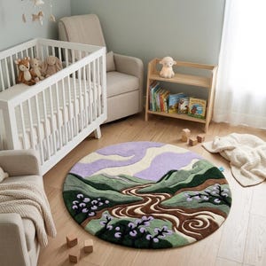 May include: A circular nursery rug with a landscape design. It features a river, mountains, and trees in green, brown, and purple. The rug is on a light wood floor in a nursery, with a cot, chair, and bookshelf visible.