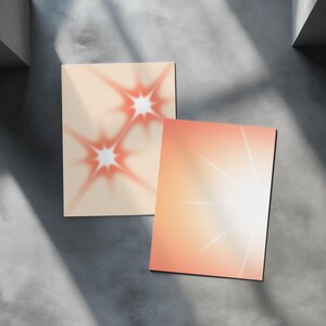 May include: Two rectangular art prints with abstract designs. One print features two red starbursts on a beige background. The other print has a gradient of orange and white with white lines radiating from the center.