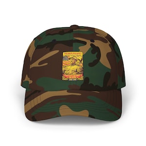 May include: A camouflage baseball cap featuring a rectangular graphic on the front. The graphic depicts Theodore Roosevelt in military attire with an American flag, the text "THEODORE ROOSEVELT", "SPEAK SOFTLY AND CARRY A BIG STICK", and "1858-1919".