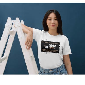 May include: White t-shirt with a black graphic that reads "DON'T WORRY, I'M A MILLENNIAL. I LEARNED CRISIS MANAGEMENT FROM A PIXELATED WAGON." The graphic features a wagon and a unicorn.