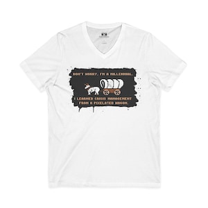 May include: White V-neck t-shirt with the text "DON'T WORRY, I'M A MILLENNIAL. I LEARNED CRISIS MANAGEMENT FROM A PIXELATED WAGON." The graphic features a pixelated wagon and animals. The shirt has a tag that says "FOCUSED".