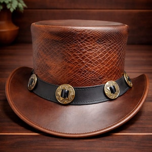 Puede incluir: Un sombrero de copa de cuero marrón con textura de piel de serpiente en la corona. El sombrero presenta una banda negra adornada con botones dorados en forma de estrella con centros negros. El ala es de un tono marrón más oscuro.