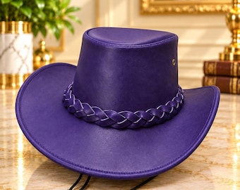 Pode incluir: Um chapéu de cowboy roxo vibrante com acabamento liso, aba larga e uma faixa trançada decorativa ao redor da copa. O chapéu inclui um cordão de queixo preto fino com um fecho ajustável e um pequeno ilhó metálico na lateral.