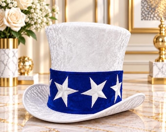 May include: A white top hat with a textured, crushed velvet-like finish. The hat features a wide, vibrant blue band around the base, decorated with several embroidered white five-pointed stars evenly spaced around the circumference.