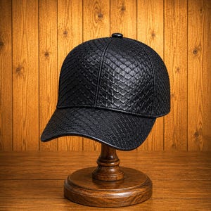 May include: A black baseball cap featuring a textured, scale-like pattern across the entire surface. The cap has a structured crown, a curved brim, and a small button at the top center. The design is uniform in color and texture throughout the piece.