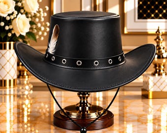Pode incluir: Um chapéu preto com topo plano e aba larga e curva. O chapéu apresenta uma faixa preta adornada com ilhós de metal prateado e uma pena castanha e branca na lateral. Um cordão preto fino para o queixo com um ajustador pende para baixo.