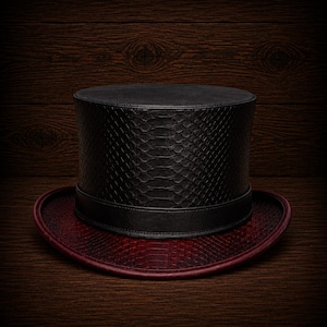 May include: A black top hat with a snakeskin texture on the crown and a burgundy snakeskin brim. The hat has a black band around the base of the crown. The hat is set against a dark wood background.