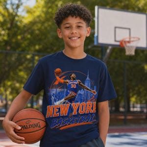 May include: A navy blue short-sleeve t-shirt featuring a graphic print of a basketball player in a blue and orange jersey dunking a ball. The design includes the text NEW YORK BASKETBALL and a silhouette of the New York City skyline.