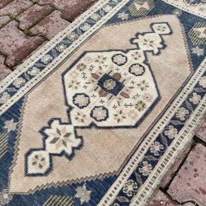 May include: A rectangular area rug featuring a central diamond-shaped medallion in beige, dark blue, and brown. The rug has a wide dark blue border with repeating floral motifs and geometric patterns, with a light beige field and intricate details.